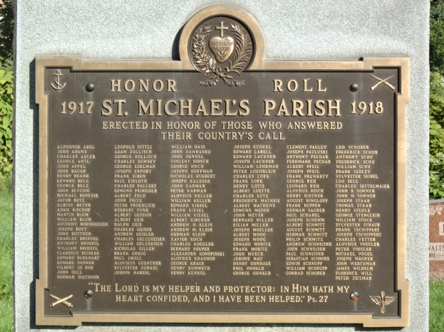 Eine Gedenktafel an einer Steinwand in der St. Michael's Parish, mit eingravierter Inschrift, umgeben von grünem Gras und Bäumen.