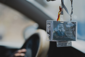 Eine Person fährt ein Auto mit einem ID-Karte am Lenkrad, ihre Hand ist auf der linken Seite sichtbar, mit einem unscharfen Hintergrund.