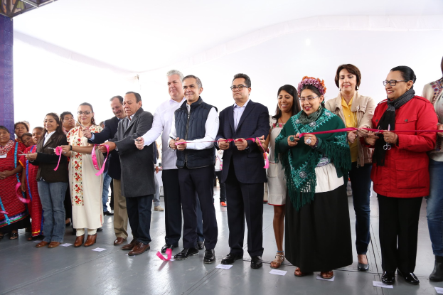 Eine Gruppe von Menschen, die eine Schnur durchschneiden, vor einer Menge stehend, mit Papieren auf dem Boden und einem weißen Tuch im Hintergrund.
