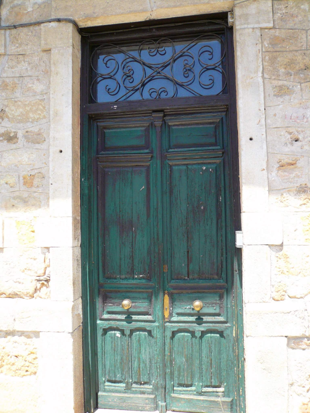 Eine grüne Tür in einem steinernen Gebäude mit einem kunstvoll verzierten Metallgitter mit Wirbeln und Kreisen oben, eingerahmt von einer Steinwand.