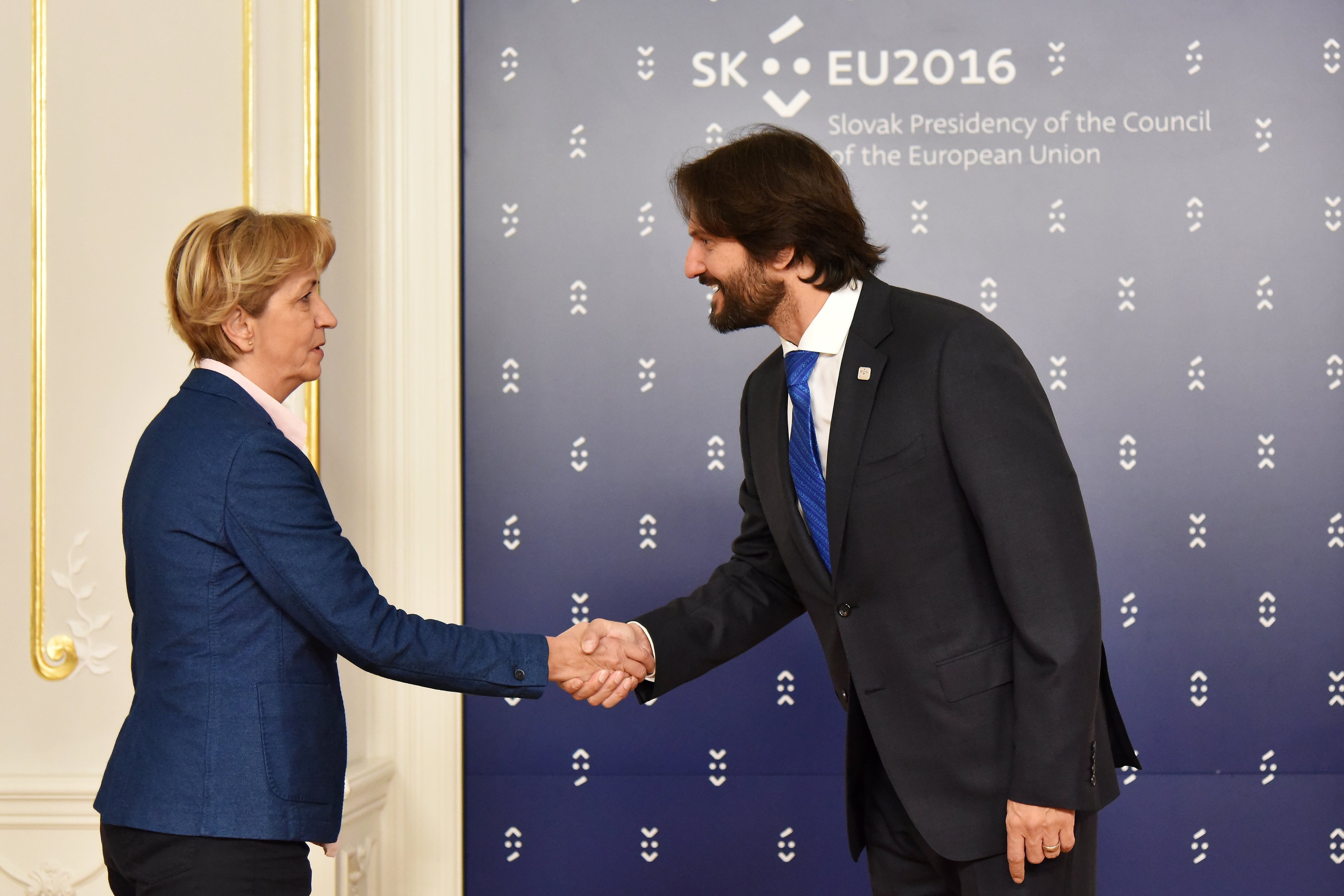 Bundeskanzlerin Angela Merkel und Bundespräsident Joachim Gauck schütteln sich die Hände vor einem "EU-Gipfel"-Plakat und lächeln freundlich.