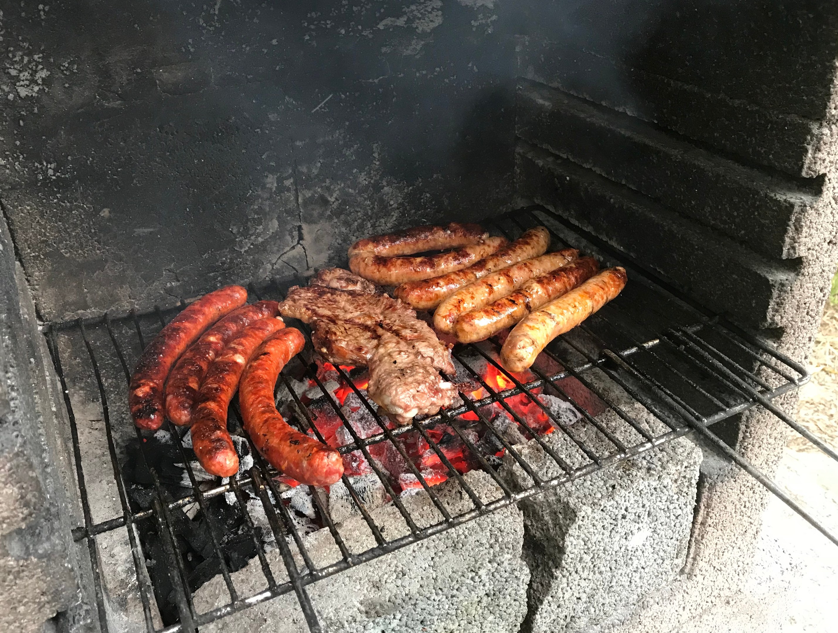 Grill mit Würstchen und Fleisch, das auf Kohle und Feuer gegrillt wird, auf Gras im Freien