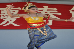 Ein Mädchen tanzt in traditioneller Kleidung und Schmuck, mit einem Banner mit Text dahinter.