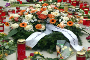 Mahnmal in Berlin mit Blumen und Kerzen vor einer Wand.